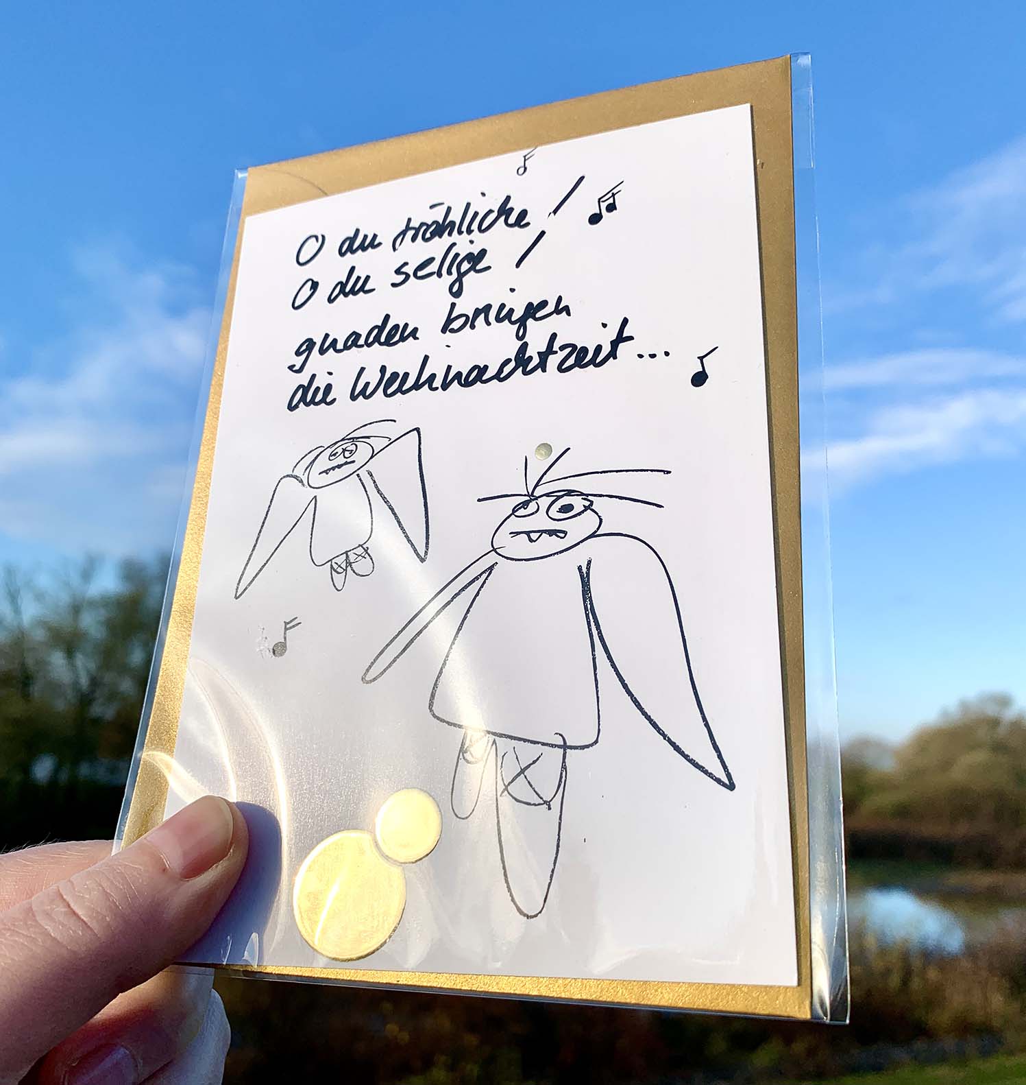 Weihnachtskarte „O du fröhliche… müde Engel“ mit goldenem Kuvert – stilvolle und humorvolle Postkarte für Weihnachten und Engel-Liebhaber. Frontansicht  mit Goldglanz