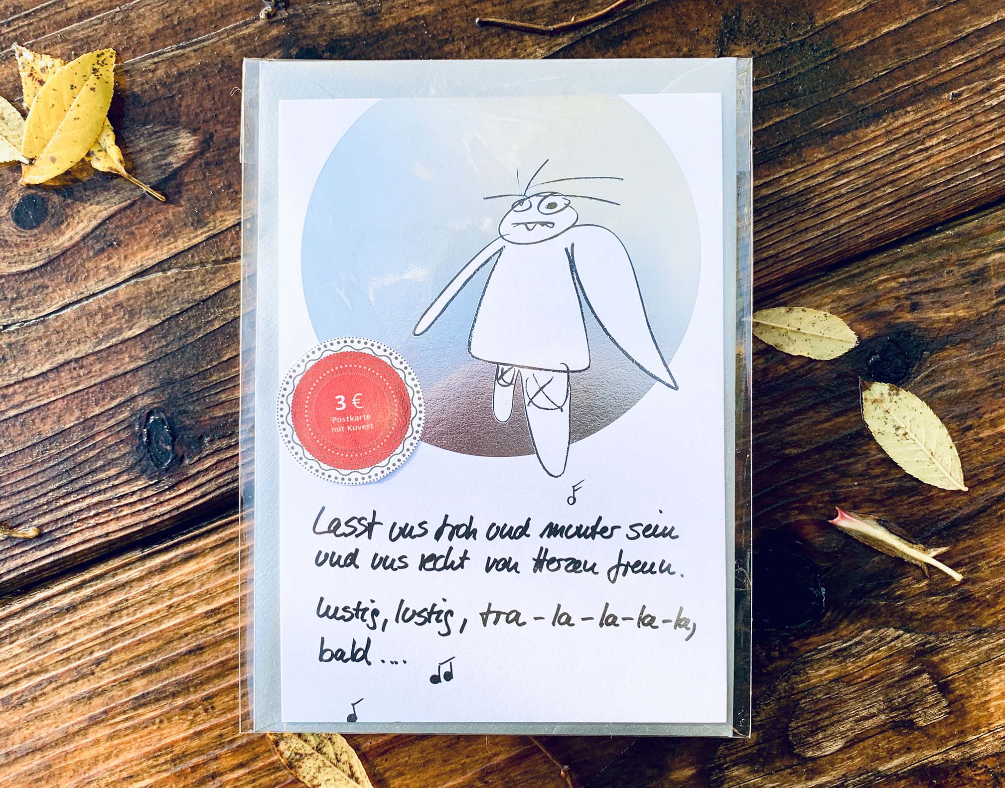 Weihnachtskarte „tra - la - la - la - la, bald… müder Engel“ mit silbernem Kuvert – stilvolle und humorvolle Postkarte für Weihnachten und Engel-Liebhaber. Frontansicht mit Klarsichthülle