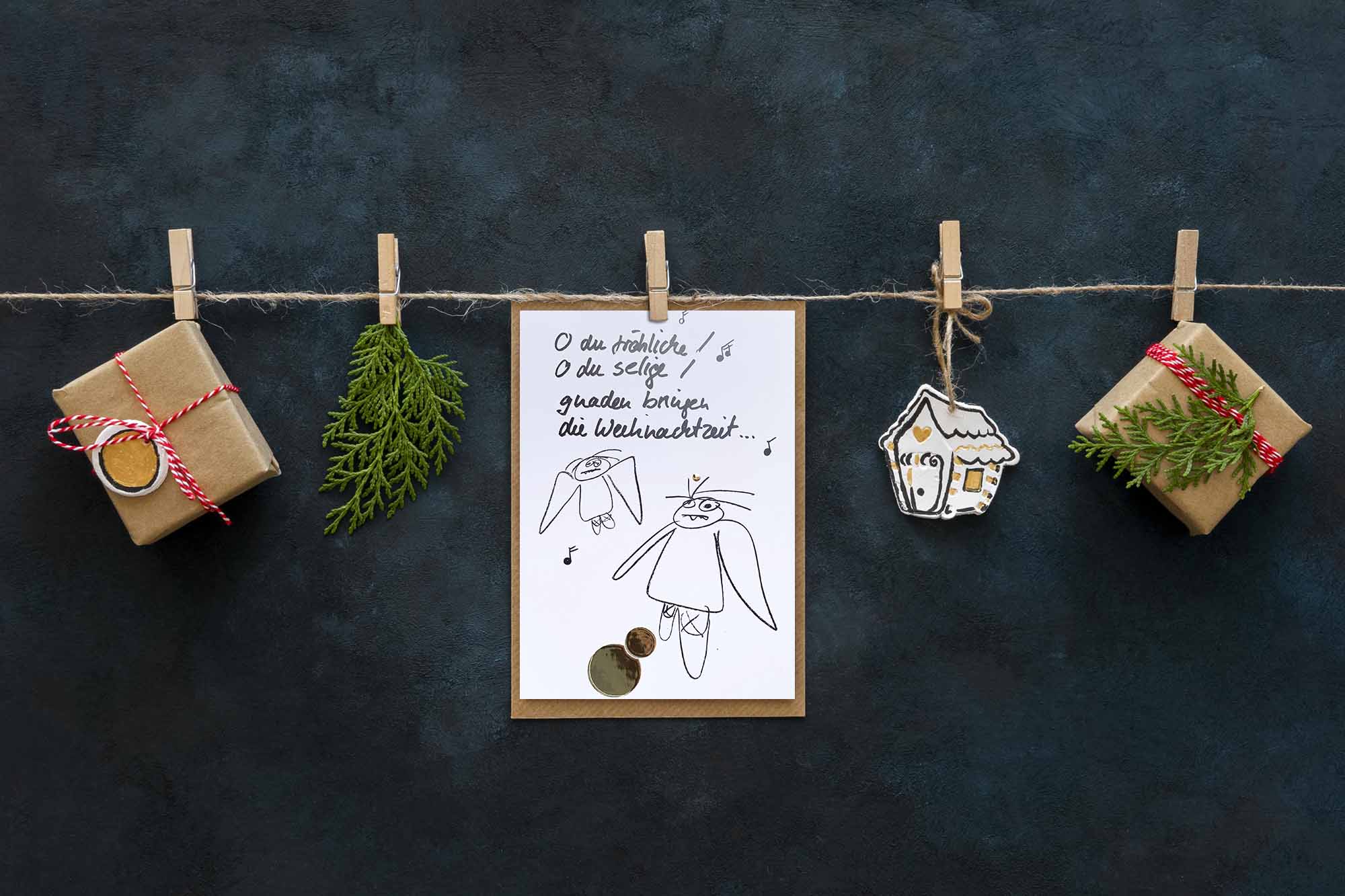 Weihnachtskarte „O du fröhliche… müde Engel“ – stilvolle und humorvolle Postkarte für Weihnachten und Engel-Liebhaber. Frontansicht mit Deko-Geschenken