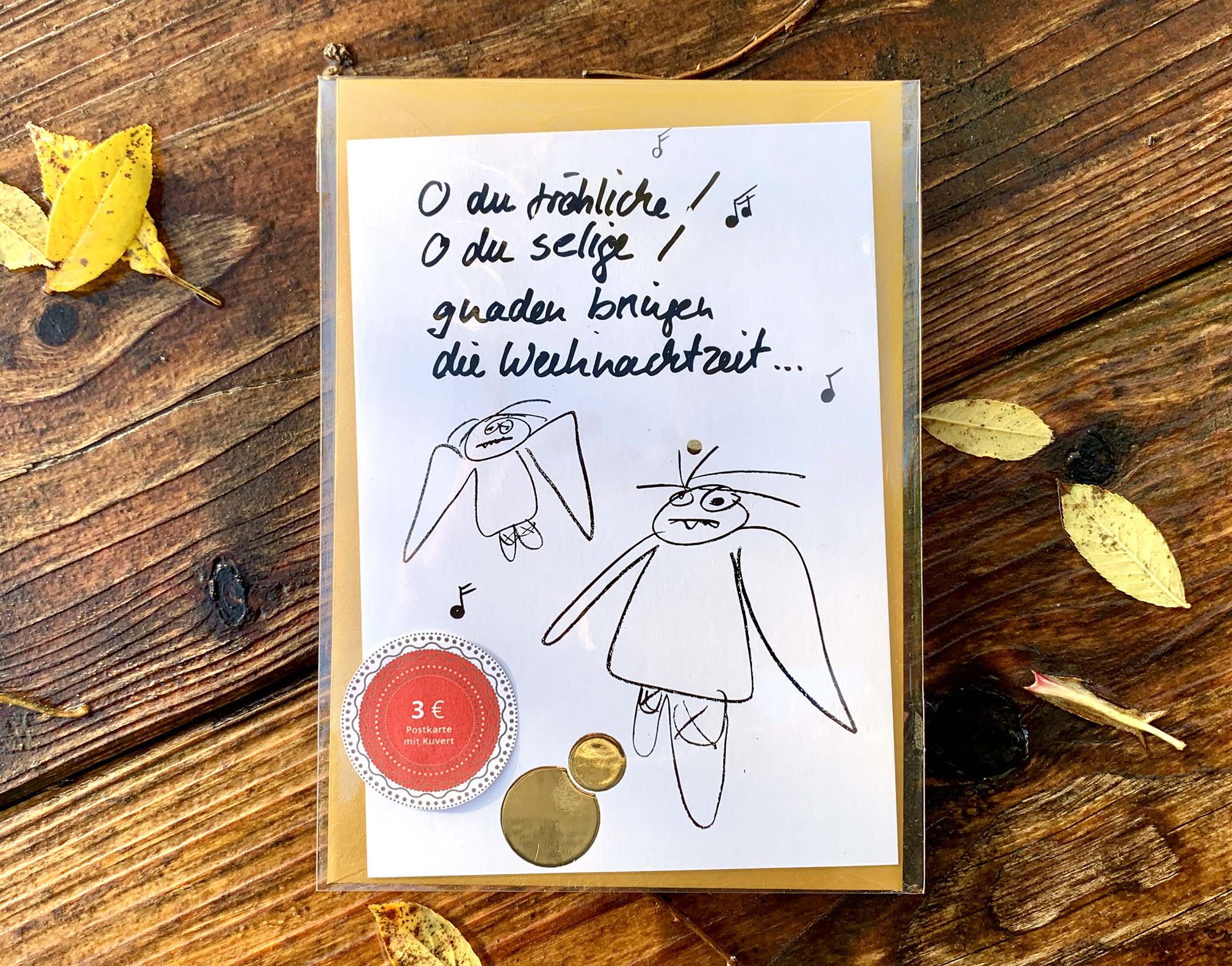 Weihnachtskarte „O du fröhliche… müde Engel“ mit goldenem Kuvert – stilvolle und humorvolle Postkarte für Weihnachten und Engel-Liebhaber. Fontansicht in Klarsichthülle